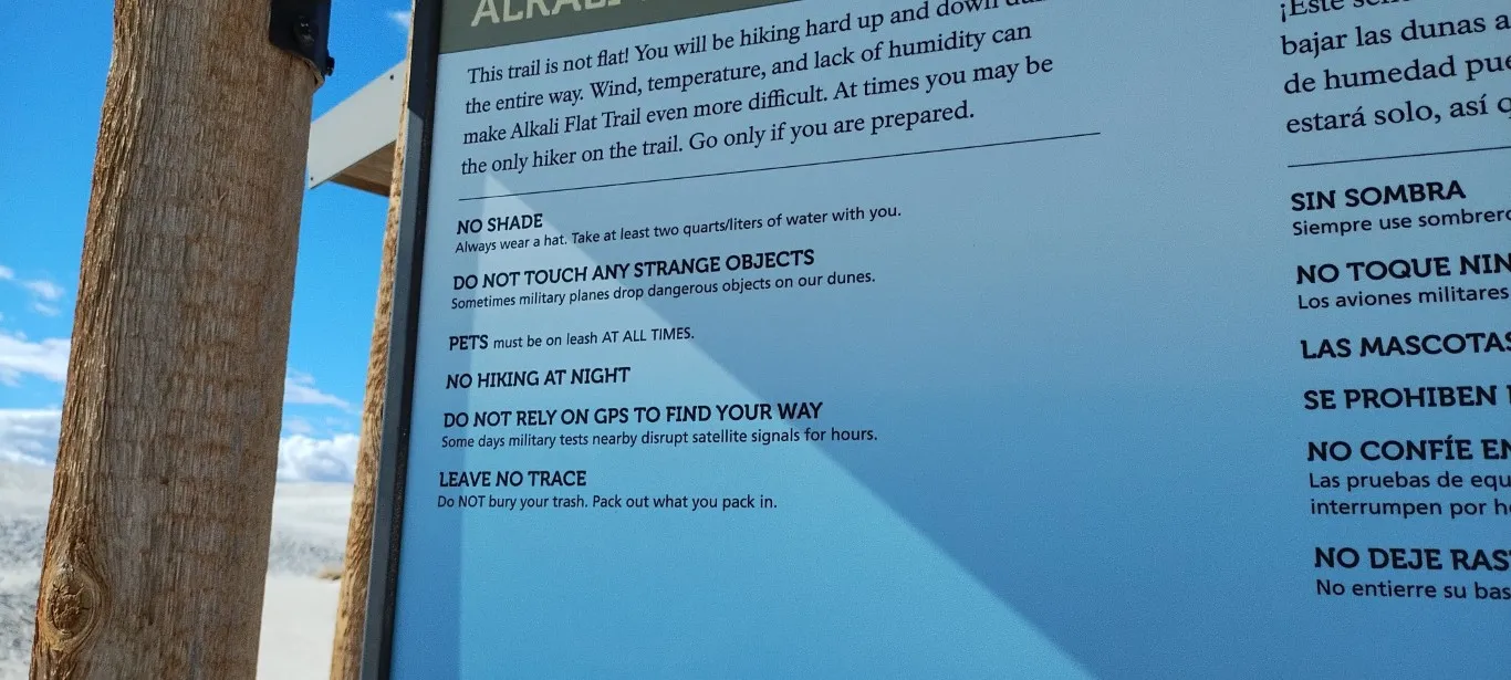 the White Sands park safety sign instructing visitors to wear a hat, avoid touching strange objects, keep pets on a leash, keep off the dunes at night, not rely on GPS due to military satellite interference, and avoid littering